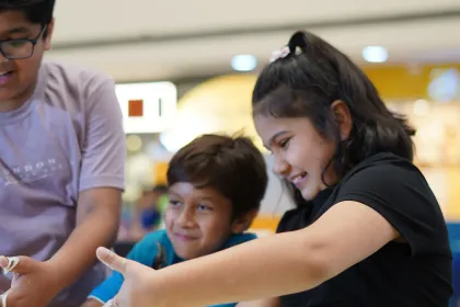 Two children reaching for a drifting bubble across a mall activity table