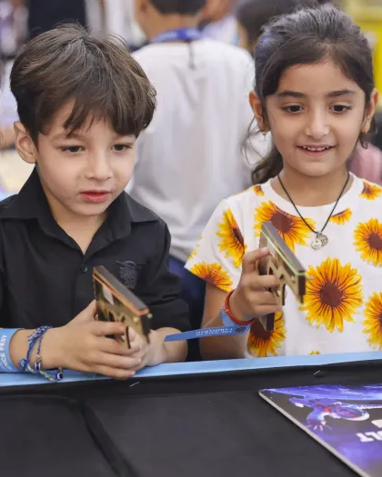 Two children examining the wooden model they have just built at a MakerMasti science table