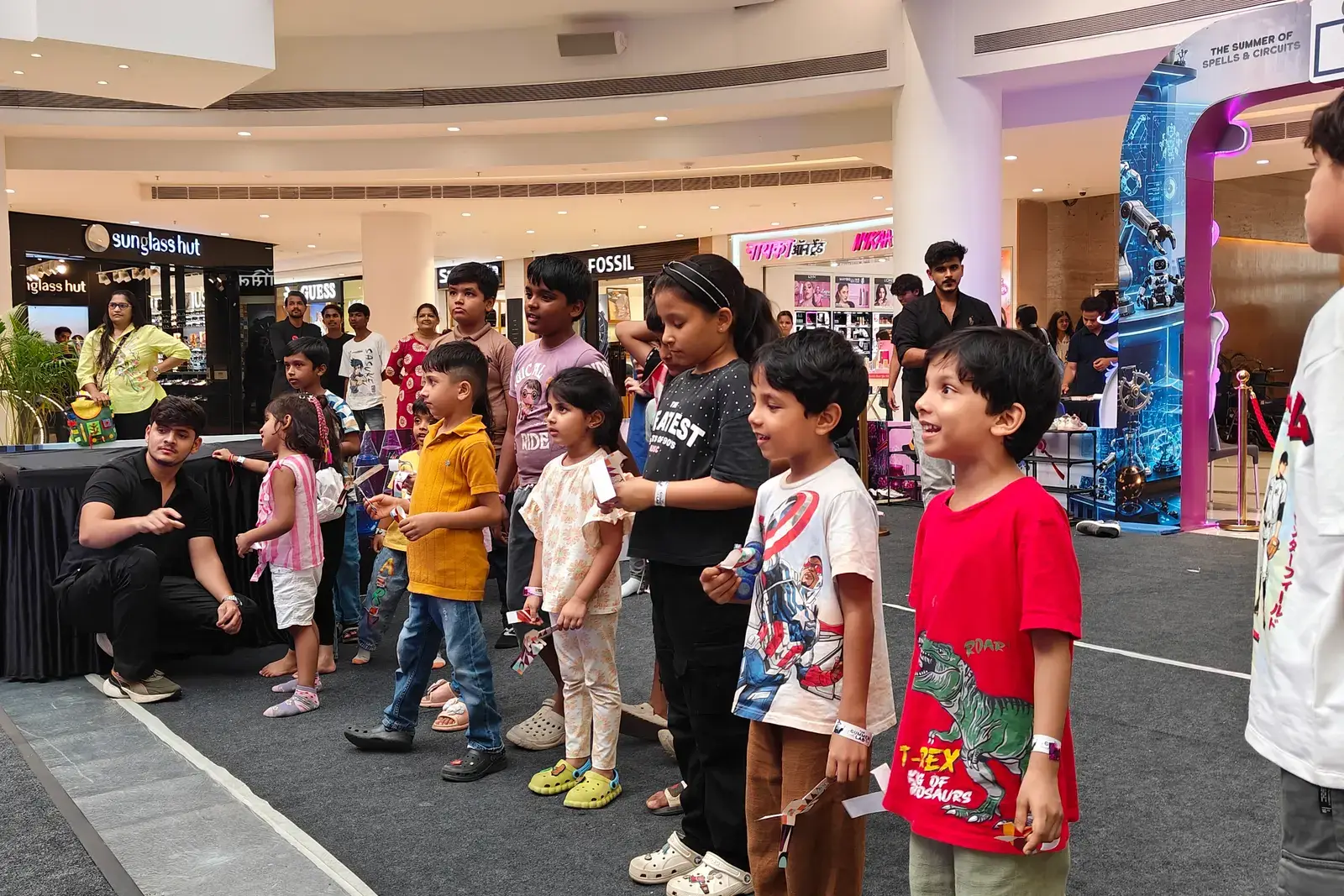 Children lining up along a mall concourse for a MakerMasti activity, storefronts behind them