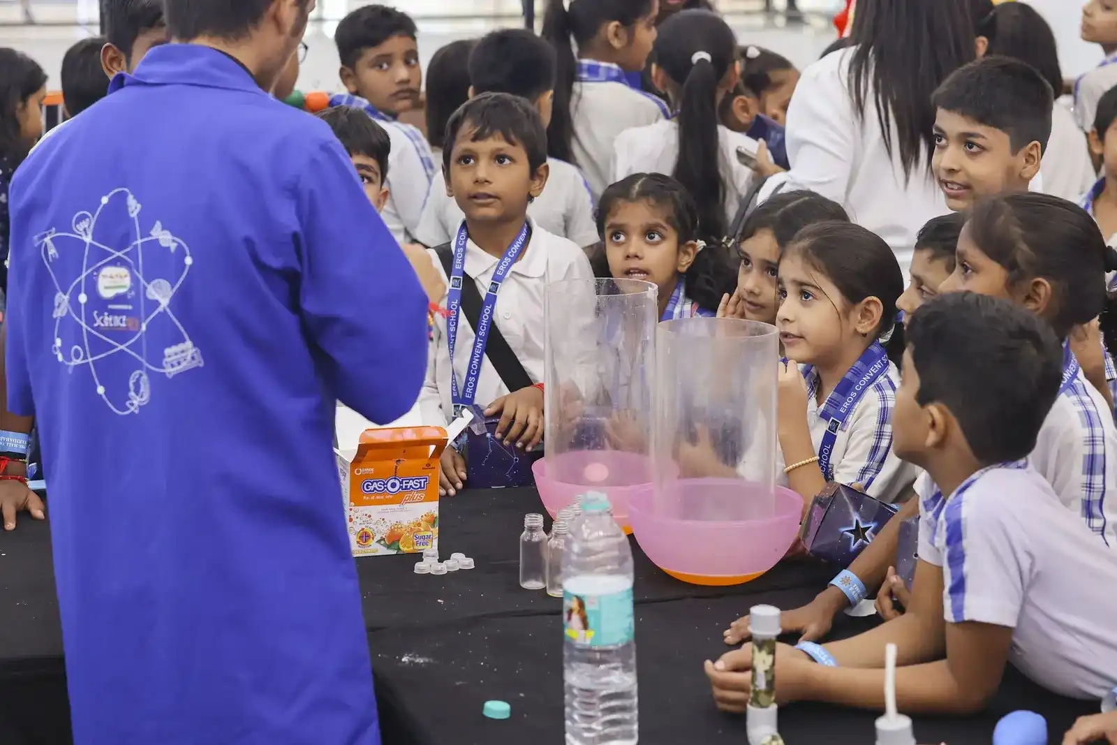 A MakerMasti science performer in a branded lab coat running a foam reaction for a ring of children