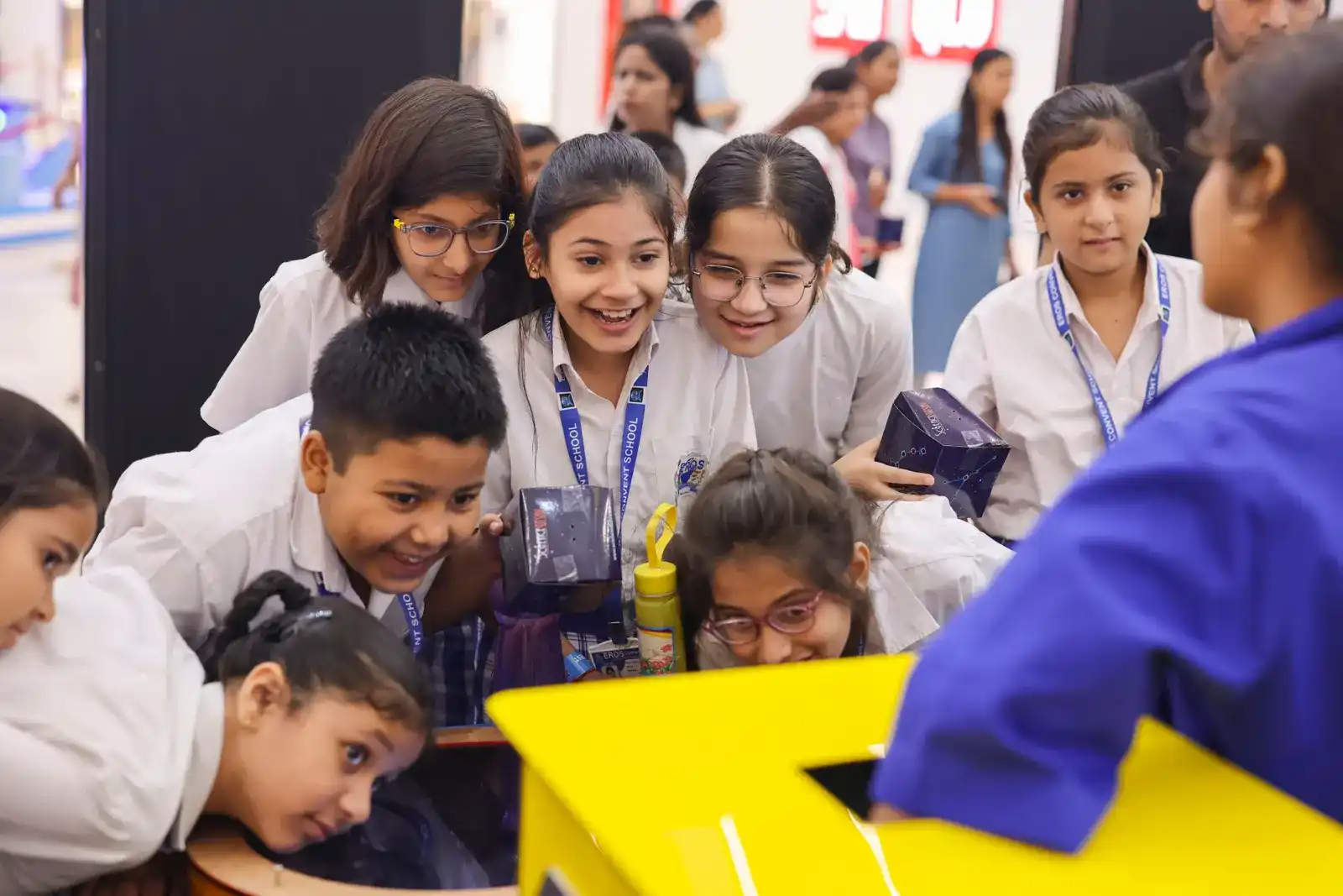 Children leaning in around a yellow funnel rig, watching an experiment take shape