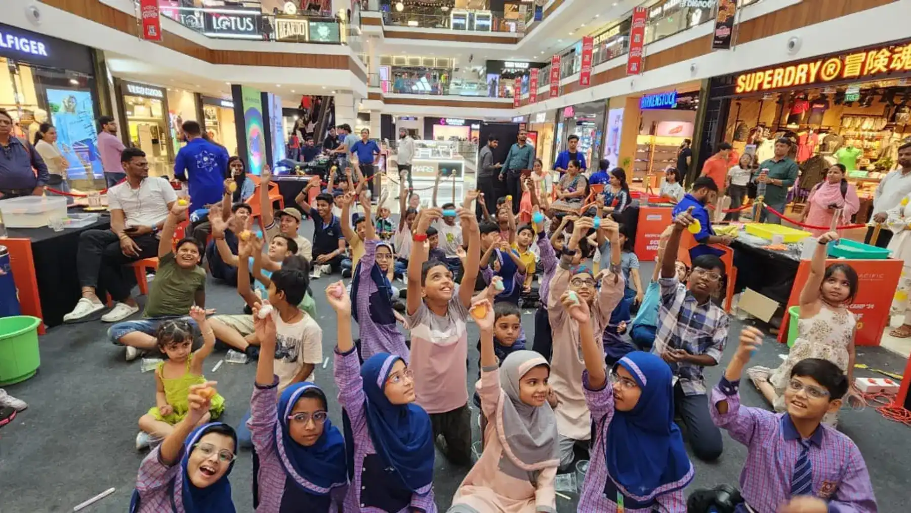 Dozens of children with their hands in the air on a packed mall floor during a MakerMasti show