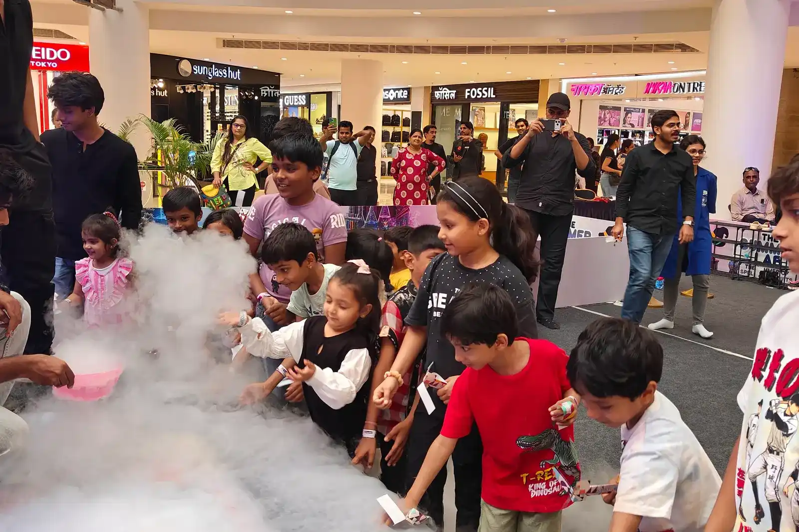 A line of children reaching into dry ice fog rolling across a MakerMasti activity counter